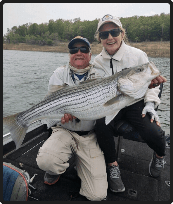 Two people holding a striped bass on the water.