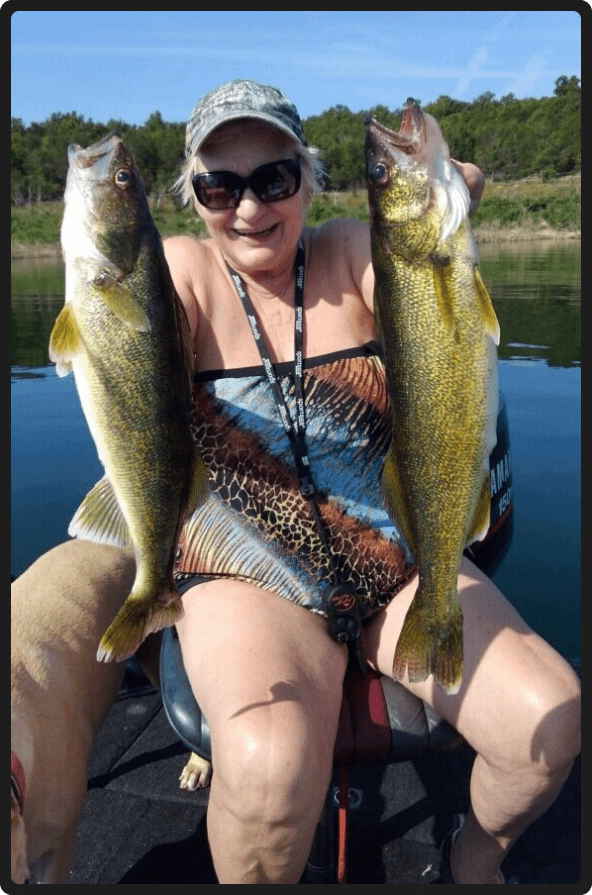 A woman holding two fish while sitting on the back of a boat.